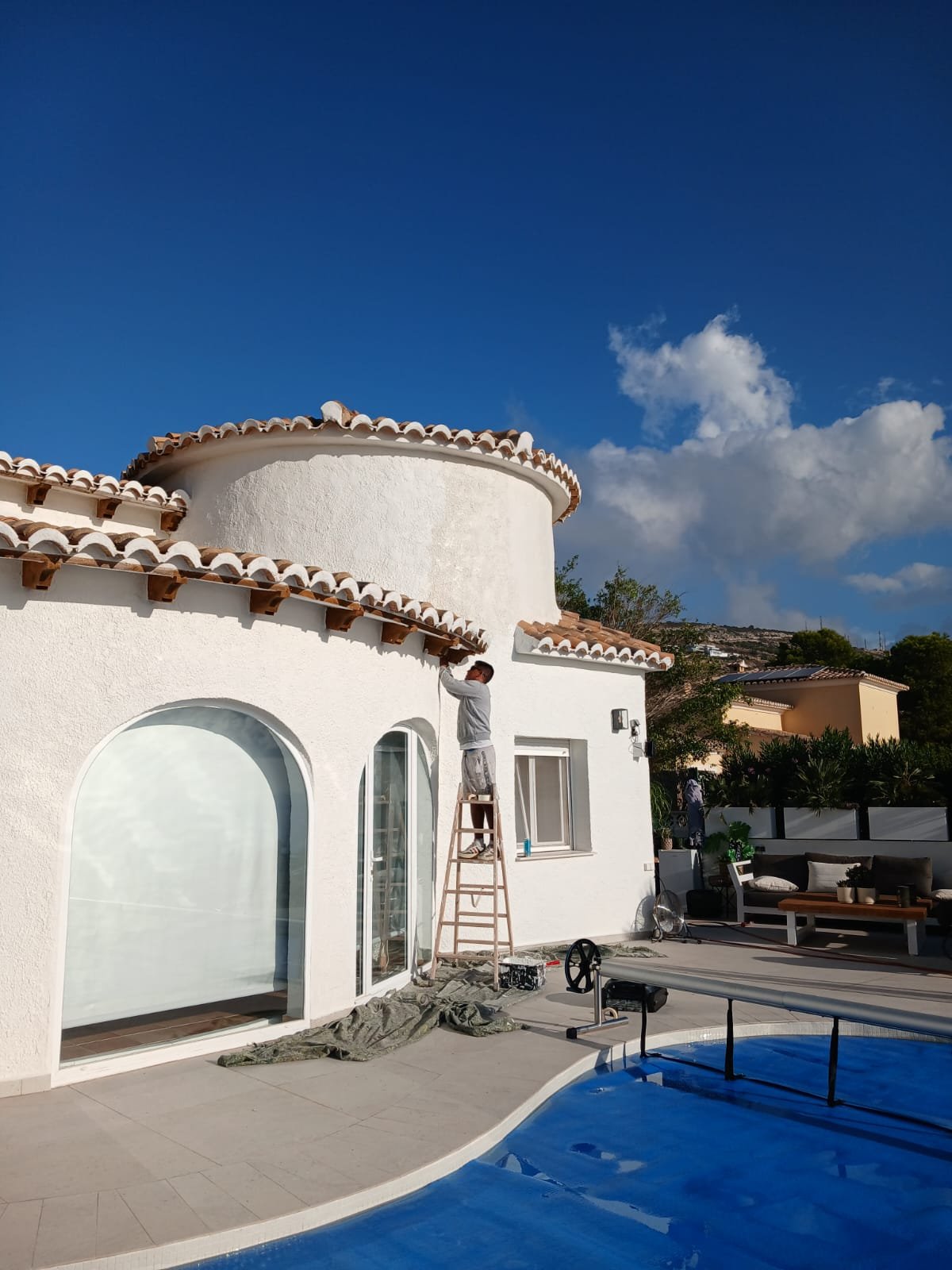 A decorator on a ladder painting the eaves of a villa, overlooking the pool — a genuine Signature Surfaces project